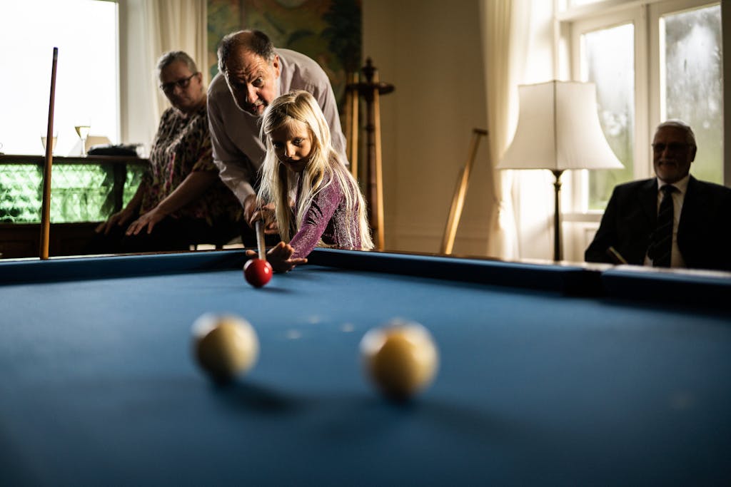 A young girl playing billiards with her supportive grandparents indoors.