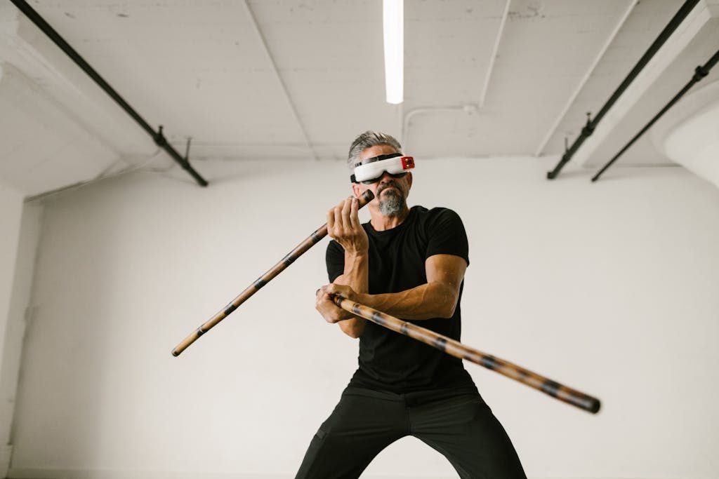Elderly man practicing arnis using wooden sticks. Indoors with VR glasses.
