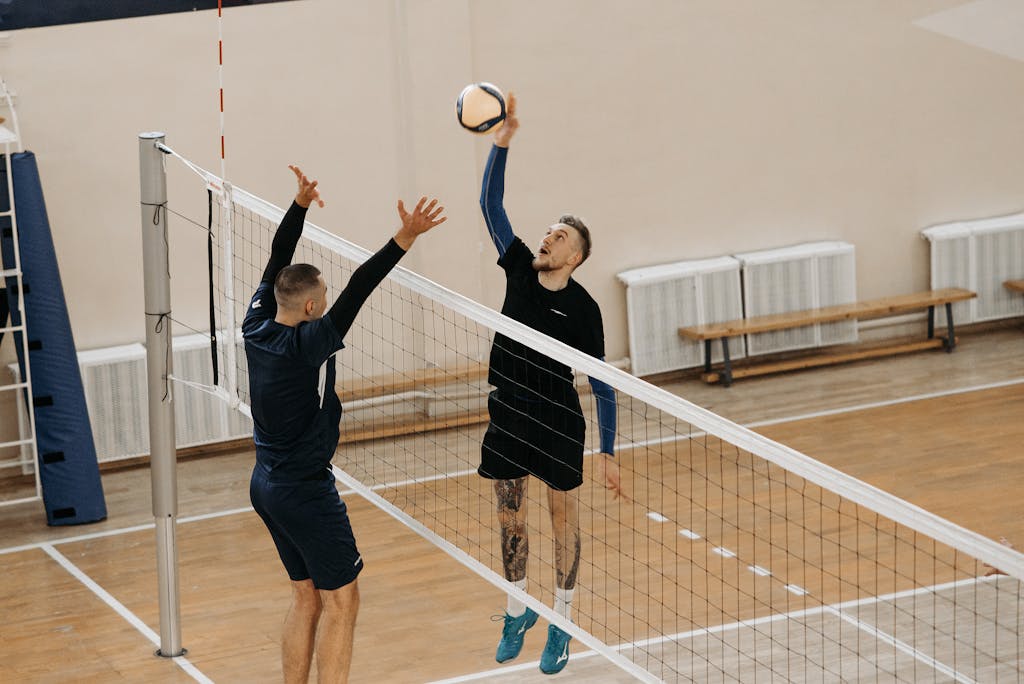 Two male athletes playing a competitive volleyball game indoors.